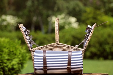 Photo of Picnic basket with blanket on wooden table in garden