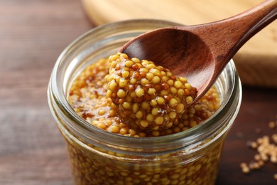 Photo of Taking whole grain mustard with spoon from jar on table, closeup