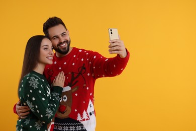 Photo of Happy young couple in Christmas sweaters taking selfie on orange background. Space for text
