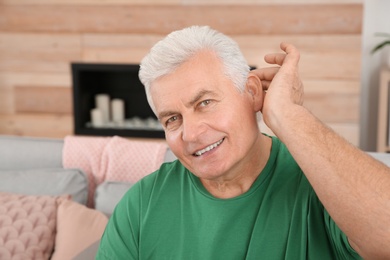 Mature man adjusting hearing aid at home