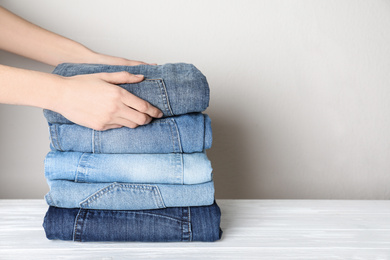 Woman folding stylish jeans on white wooden table, closeup. Space for text