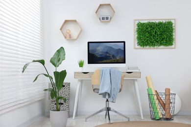 Green artificial plant wall panel and desk with computer in light room. Interior design