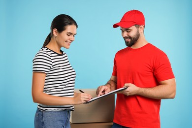 Photo of Smiling courier showing woman where sign order receipt on light blue background