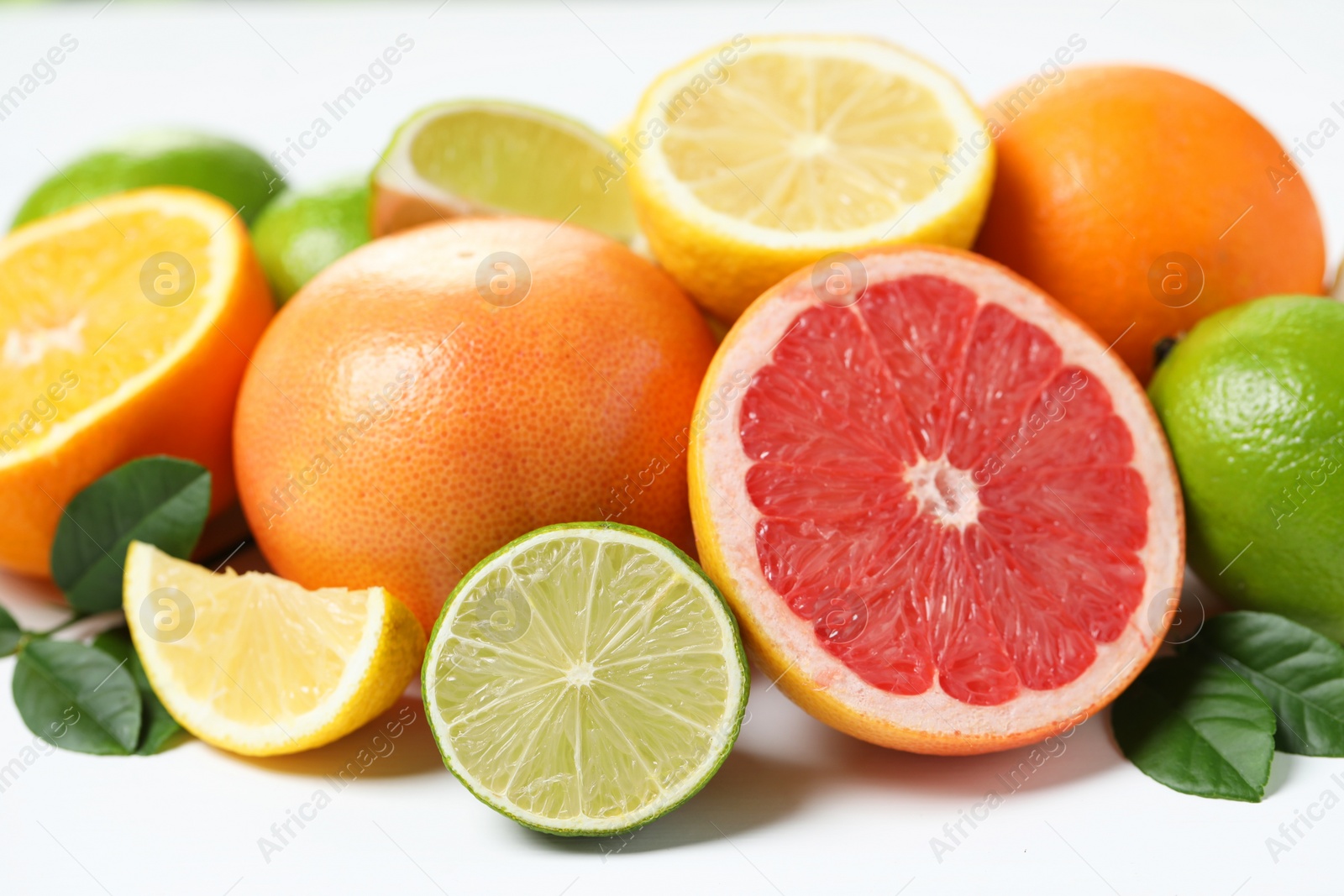 Photo of Different fresh citrus fruits and leaves on white table, closeup