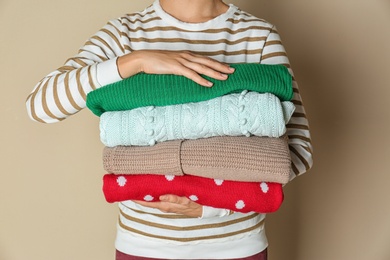 Photo of Woman holding stack of winter clothes on color background