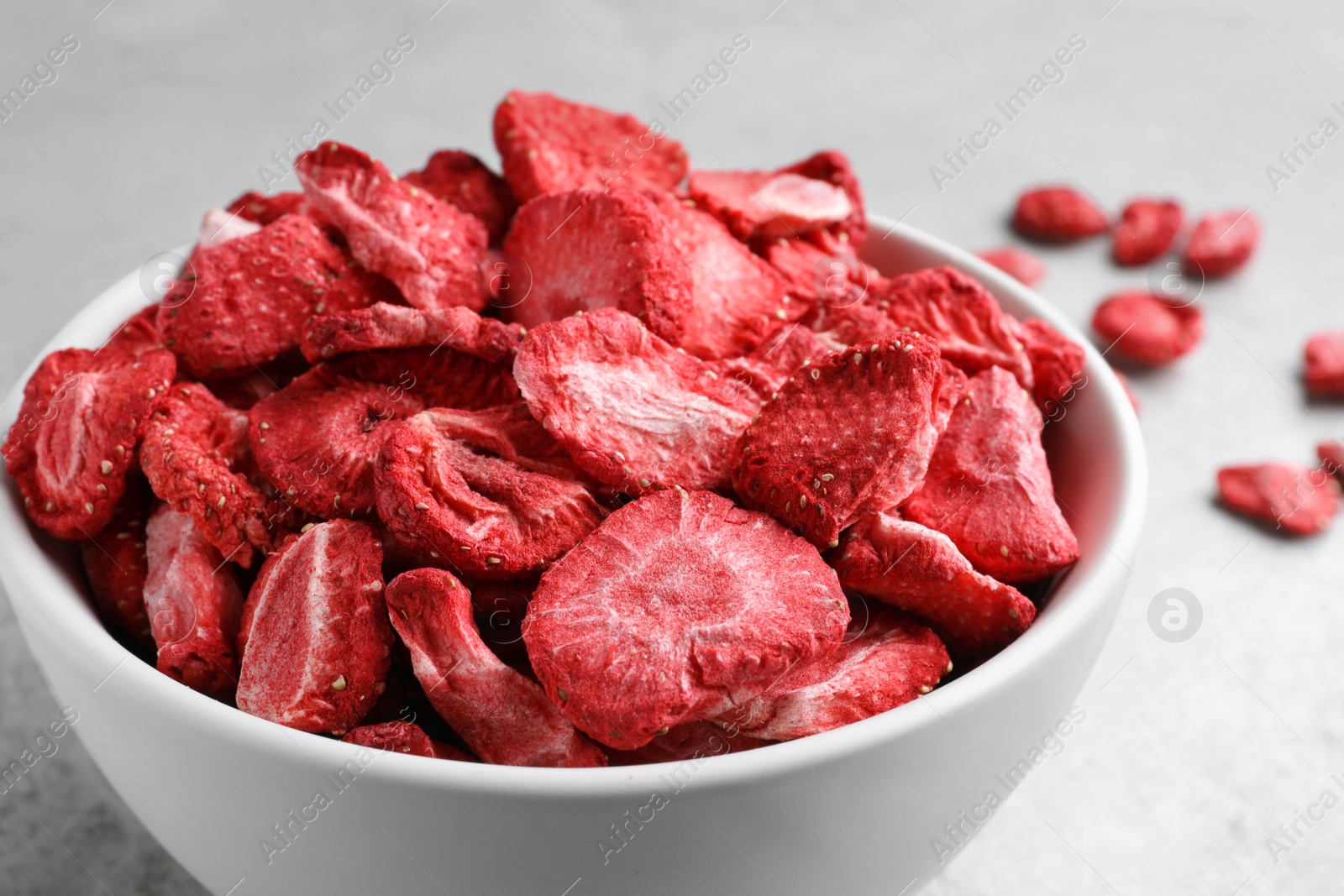 Photo of Bowl with dried strawberries on light grey table, closeup