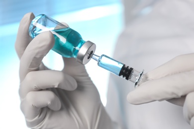Doctor filling syringe with vaccine from vial on blurred background, closeup