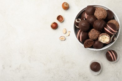 Photo of Different delicious chocolate truffles in bowl on light grey table, flat lay. Space for text