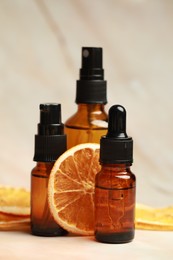 Photo of Bottles of organic cosmetic products and dried orange slices on pink marbled background