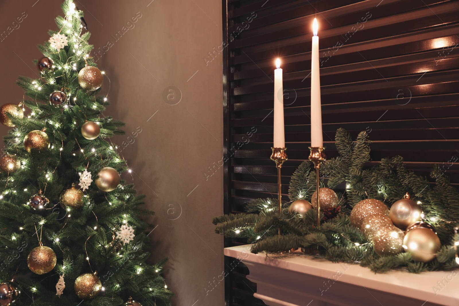 Photo of Burning candles and Christmas decor on white mantelpiece indoors