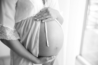 Young pregnant woman in lace nightgown on light background, closeup. Black and white effect