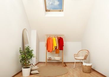 Photo of Stylish clothes rack, mirror and wicker chair in attic room. Interior design