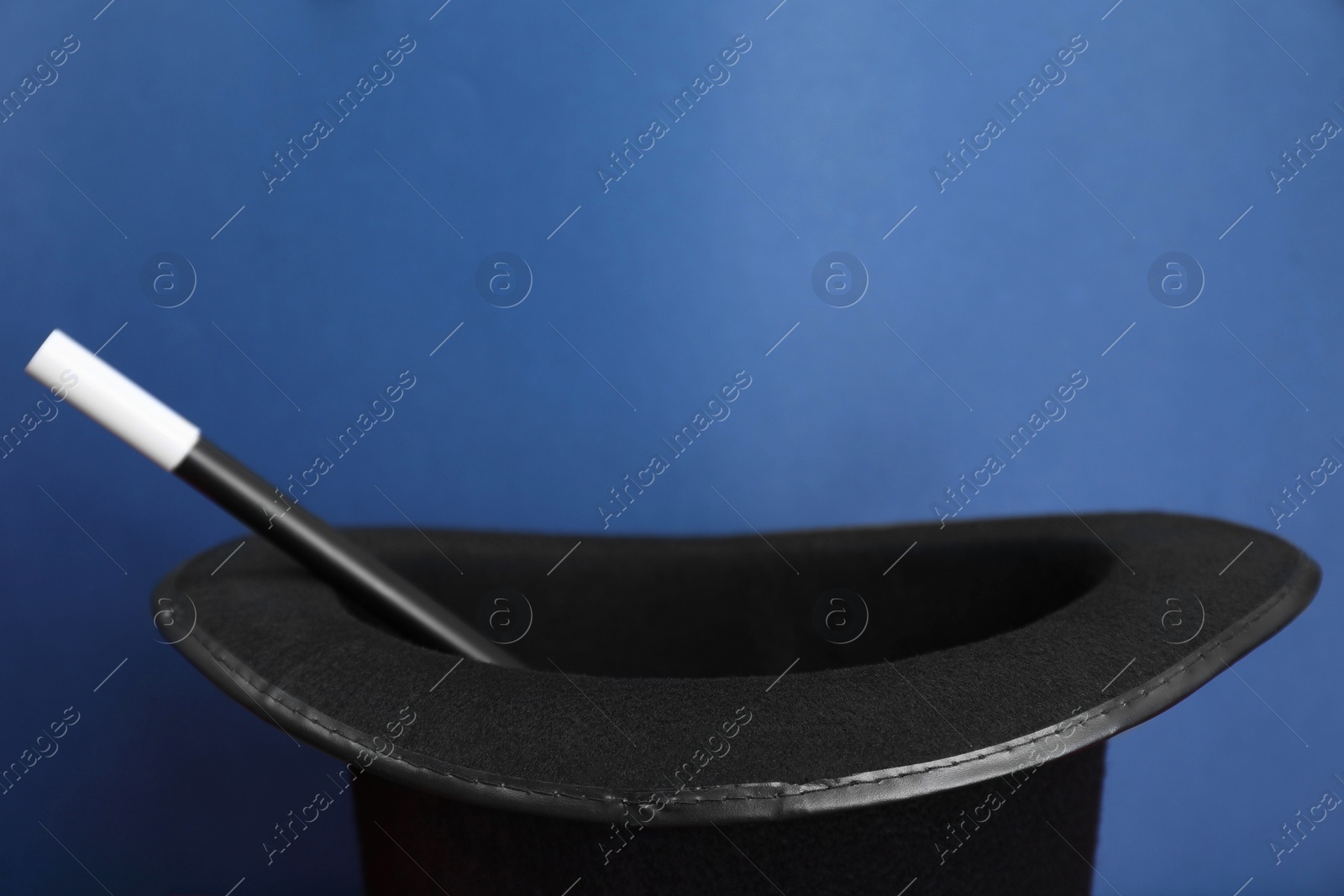 Photo of Black magician top hat and wand on blue background, closeup. Space for text