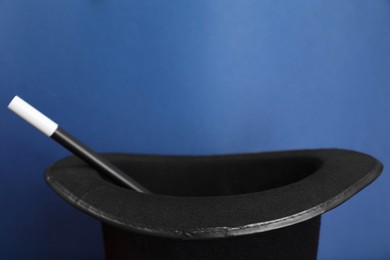 Photo of Black magician top hat and wand on blue background, closeup. Space for text
