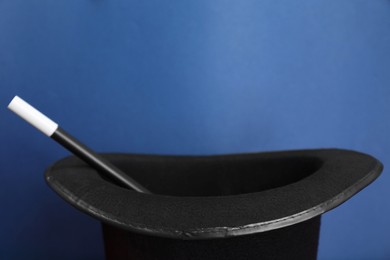 Black magician top hat and wand on blue background, closeup. Space for text