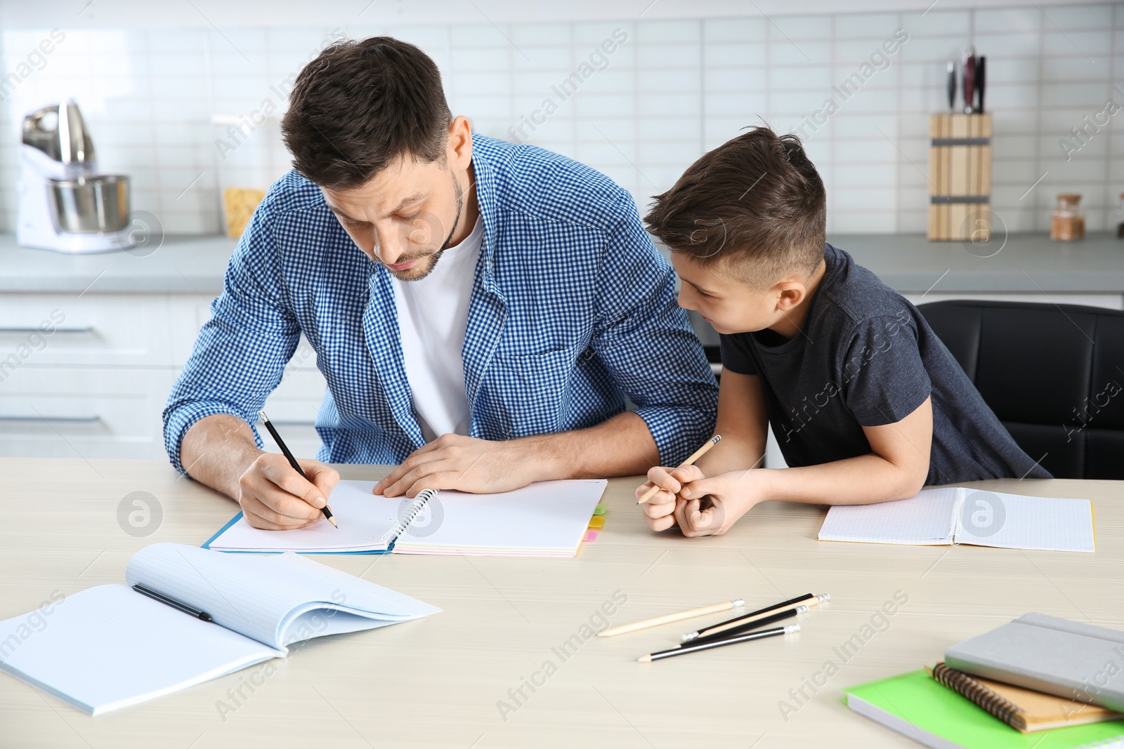 Photo of Dad helping his son with homework in kitchen