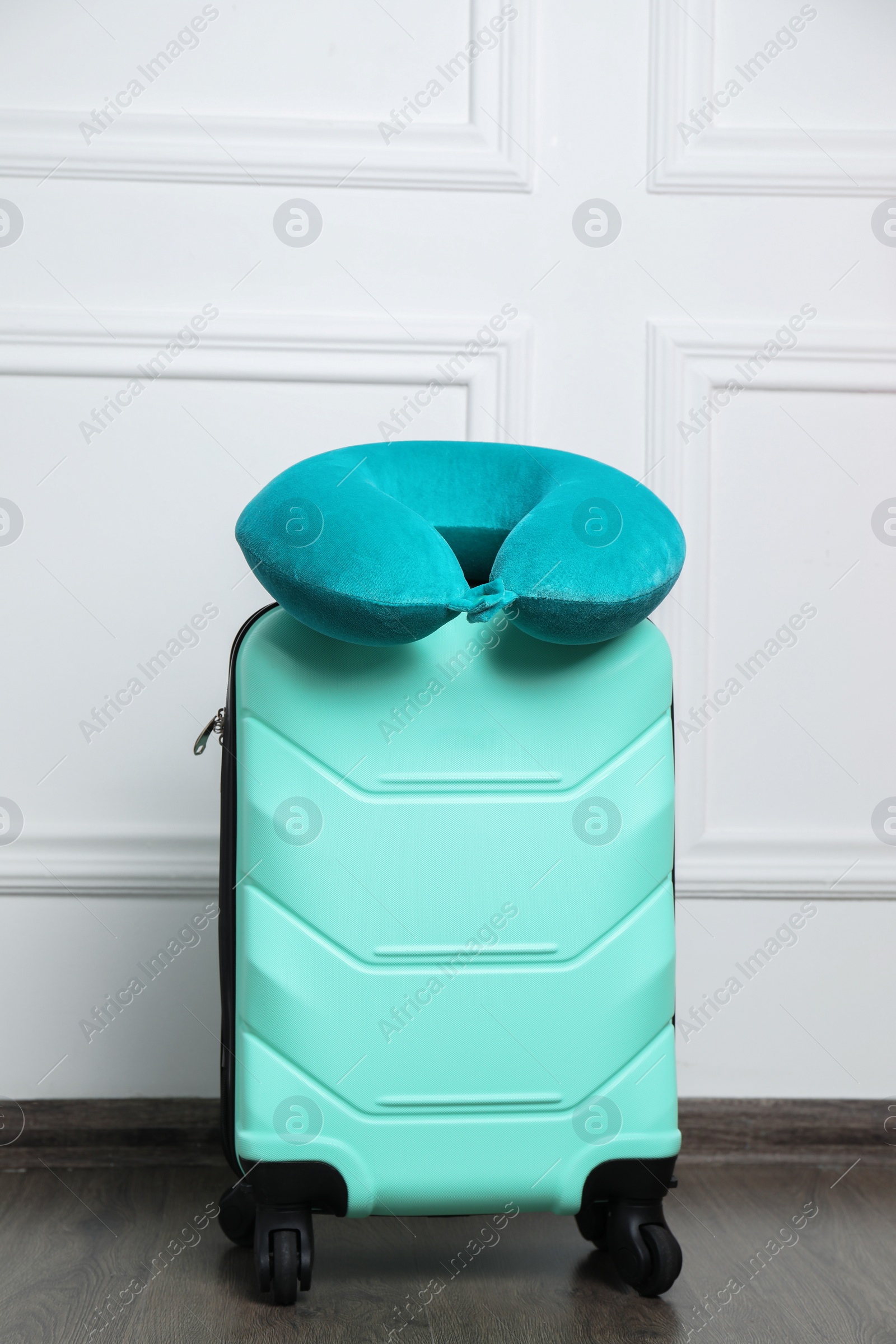 Photo of Turquoise travel pillow on suitcase near white wall indoors