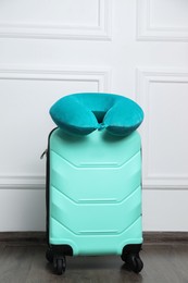 Photo of Turquoise travel pillow on suitcase near white wall indoors