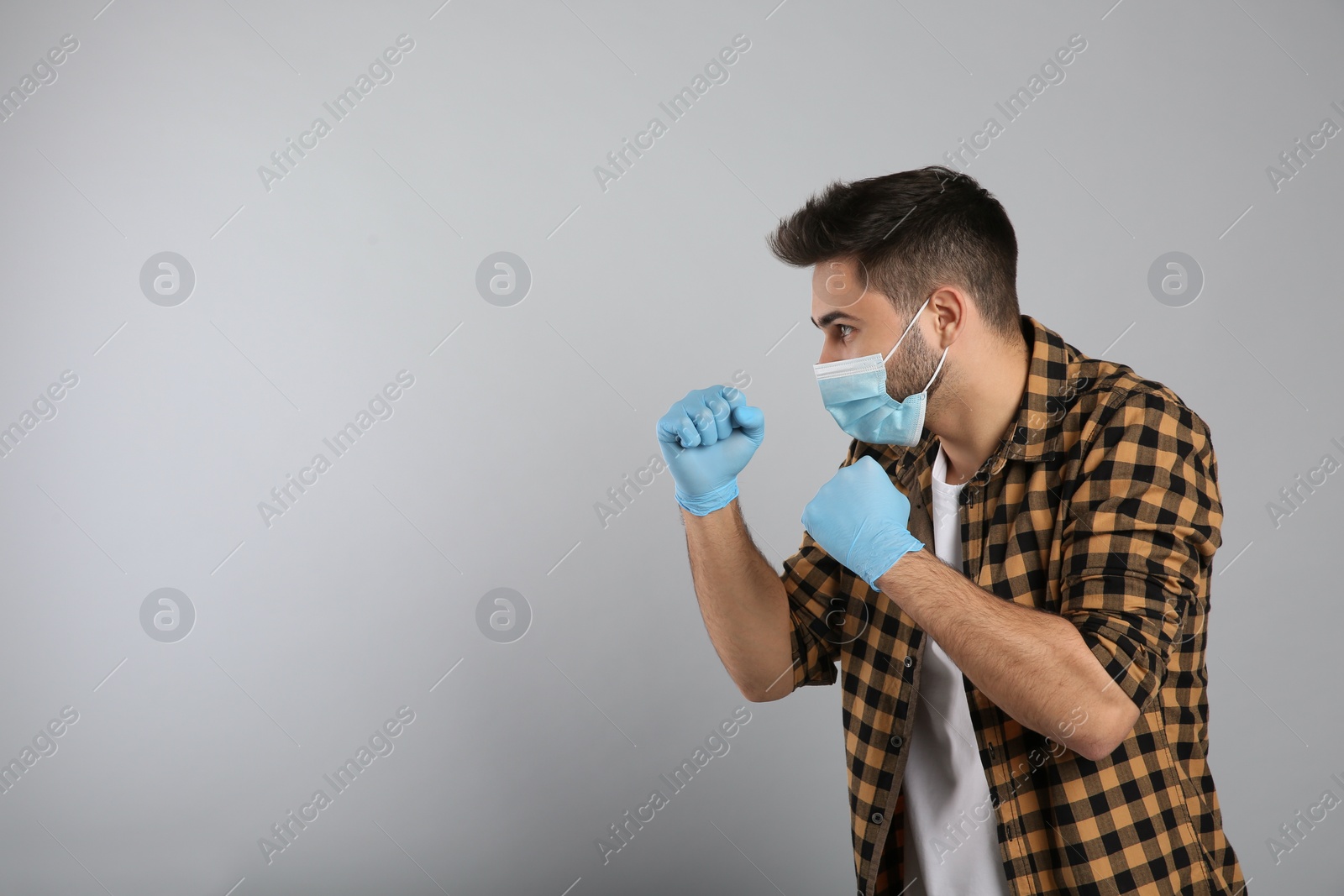 Photo of Man with protective mask and gloves in fighting pose on light grey background, space for text. Strong immunity concept