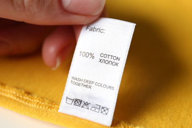 Woman reading clothing label with care symbols and material content on yellow shirt, closeup