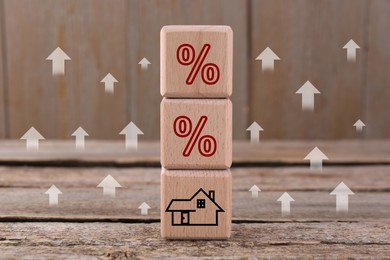 Mortgage rate rising illustrated by upward arrows and percent signs. Cubes with house icon on wooden table