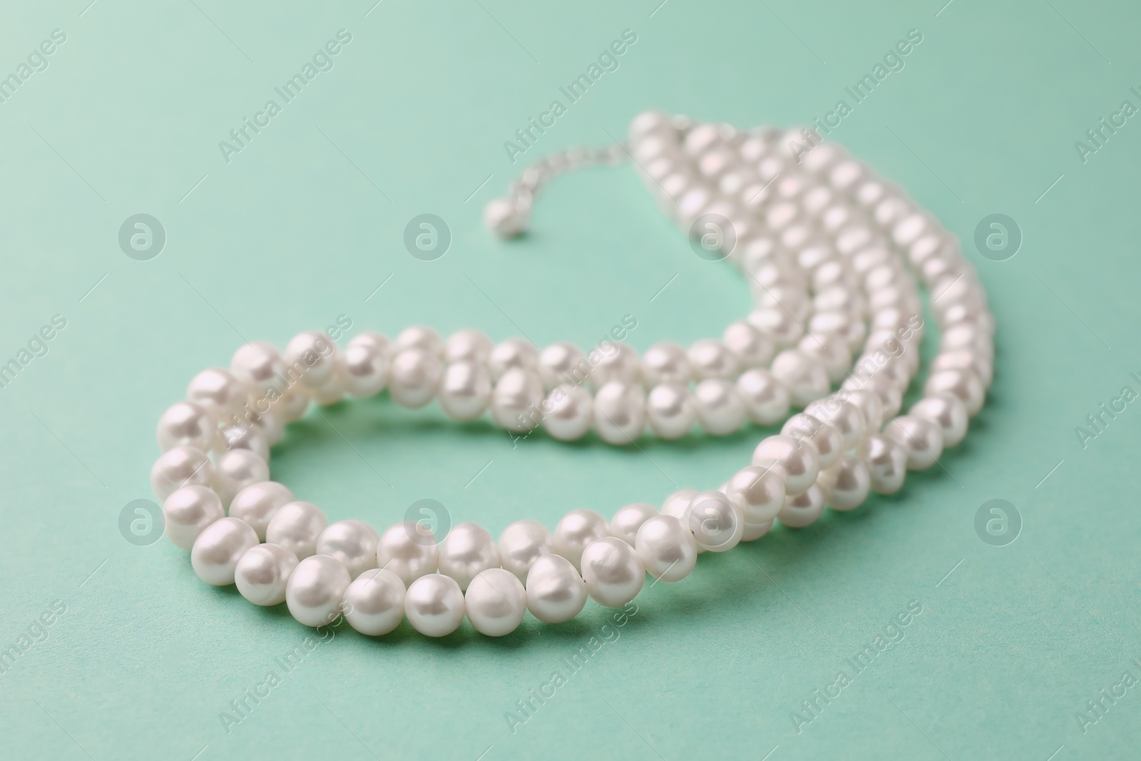 Photo of Elegant pearl necklace on turquoise background, closeup