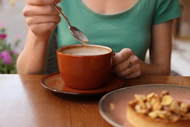 Photo of Woman with cup of coffee and delicious cake at table, closeup