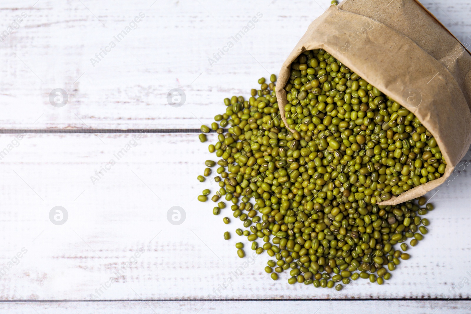 Photo of Paper bag with green mung beans on white wooden table, top view. Space for text