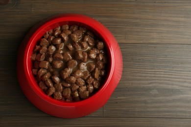 Photo of Wet pet food in feeding bowl on wooden background, top view. Space for text