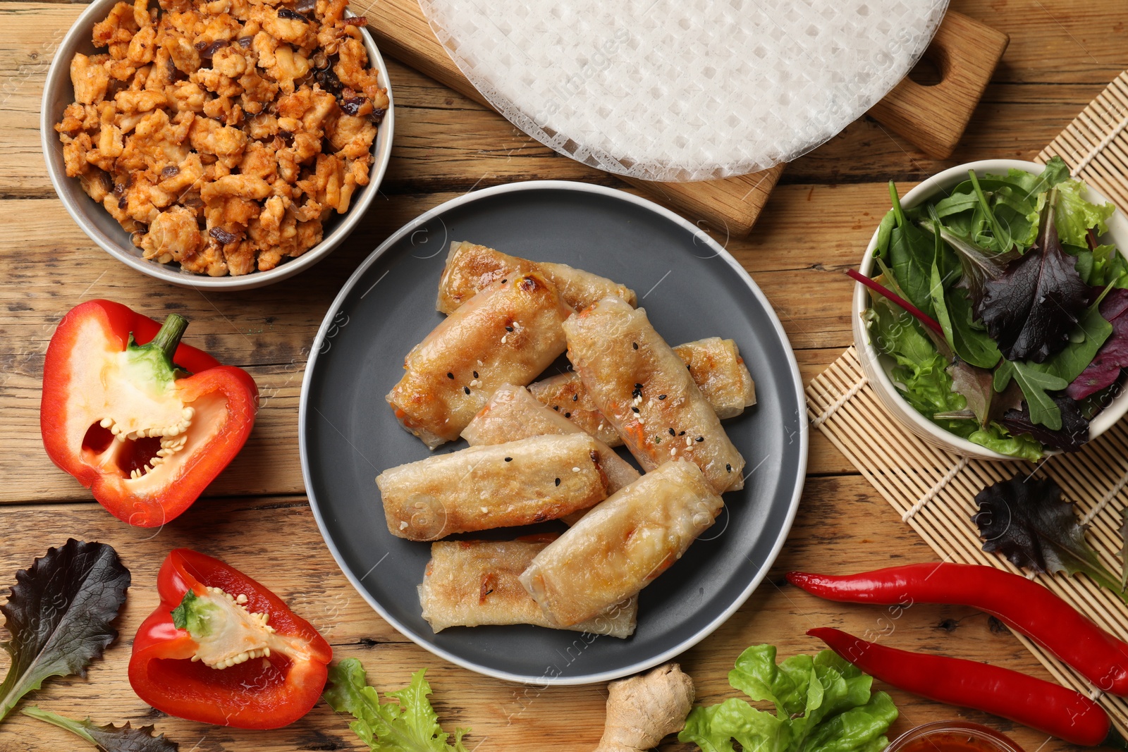 Photo of Tasty fried spring rolls and ingredients on wooden table, flat lay