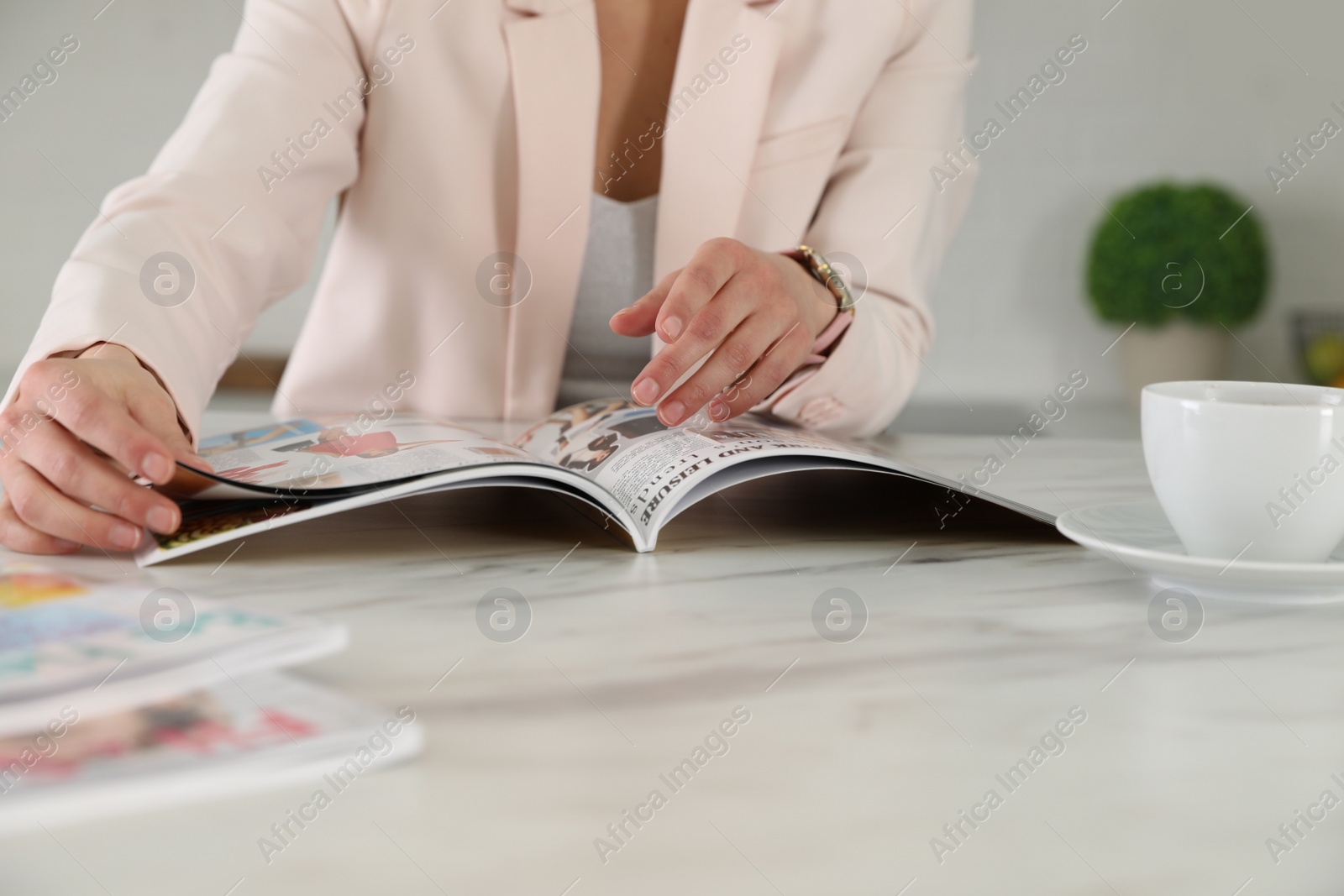 Photo of Woman with coffee reading magazine at white marble table, closeup