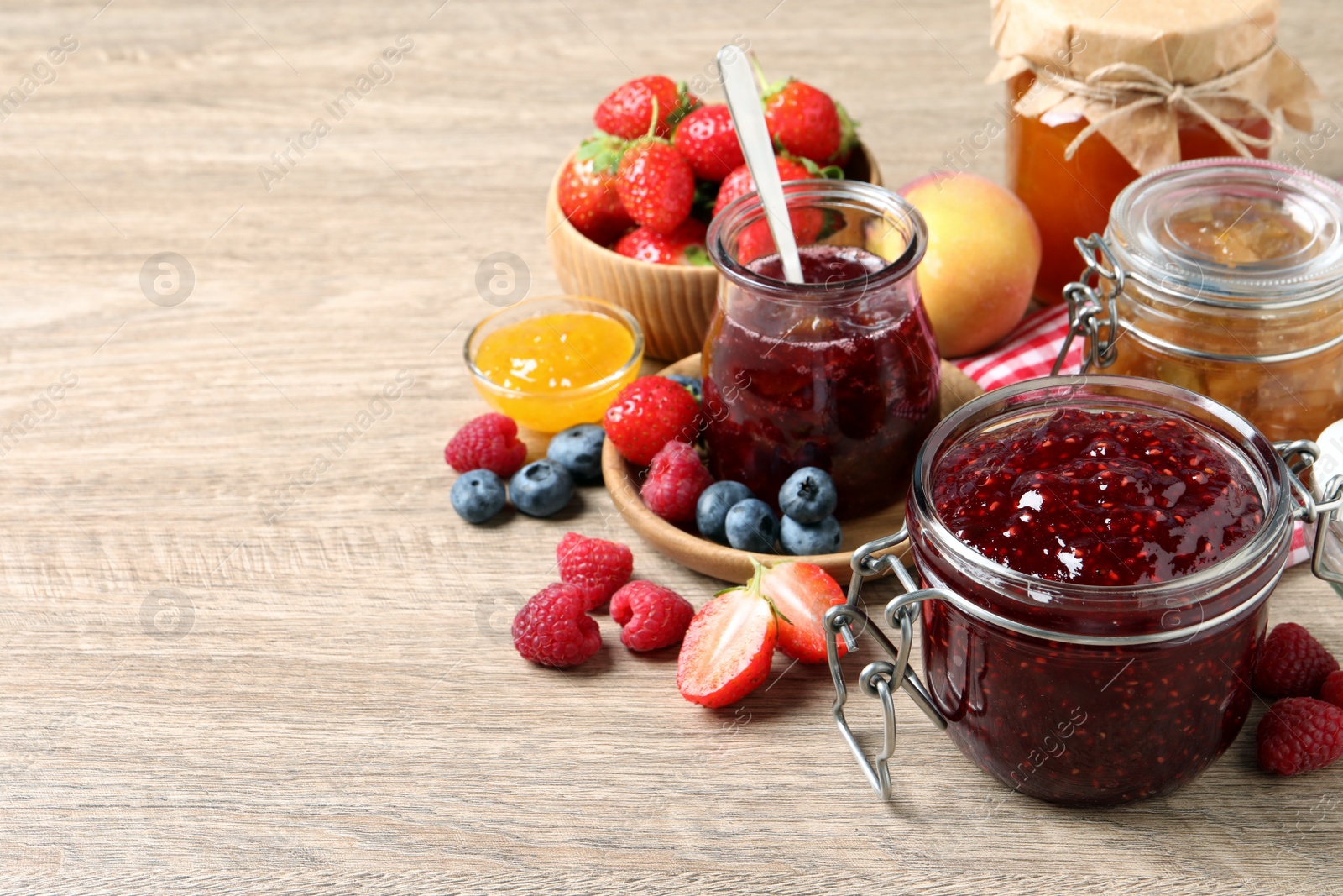 Photo of Jars with different jams and fresh fruits on wooden table. Space for text