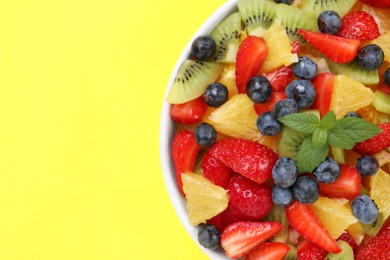 Yummy fruit salad in bowl on yellow background, top view. Space for text