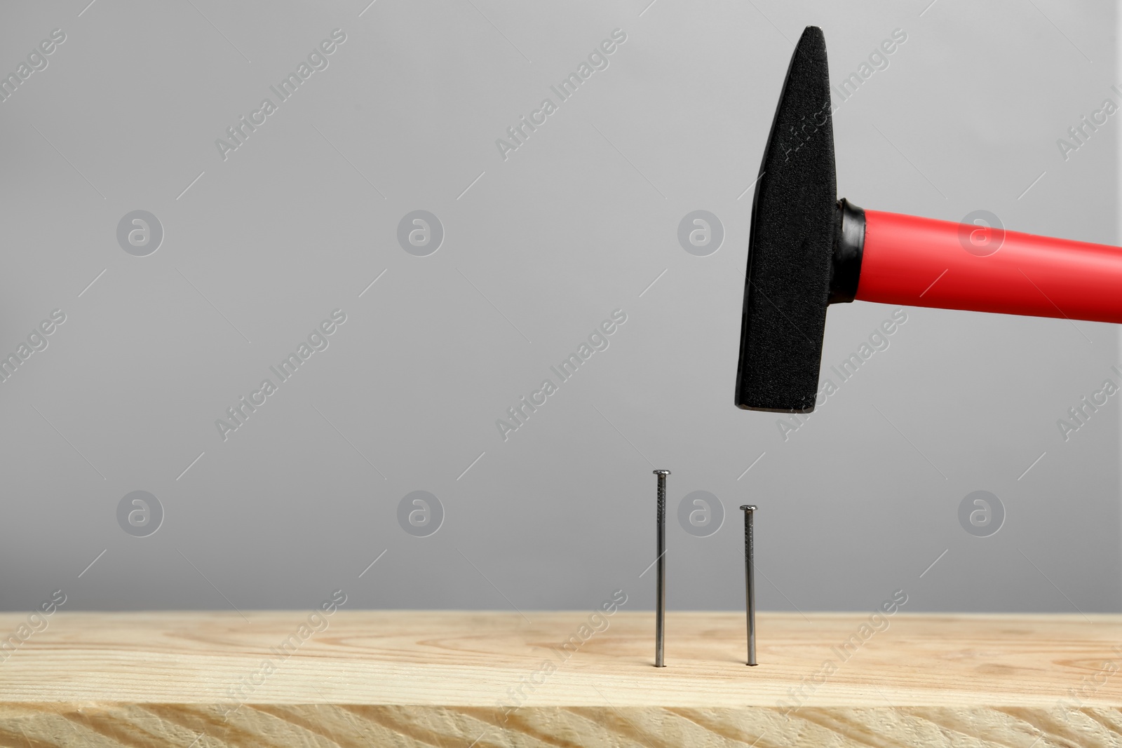 Photo of Hammering nail into wooden surface against grey  background, space for text