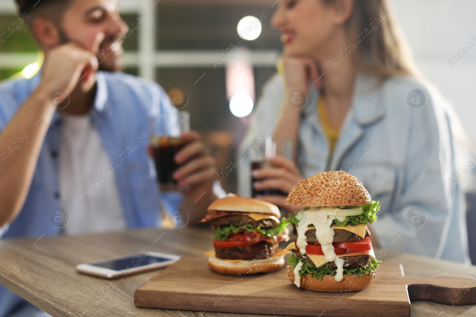 Photo of Young couple having lunch in restaurant, focus on board with burgers