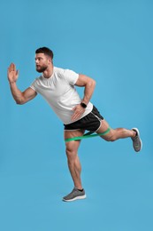 Young man exercising with elastic resistance band on light blue background