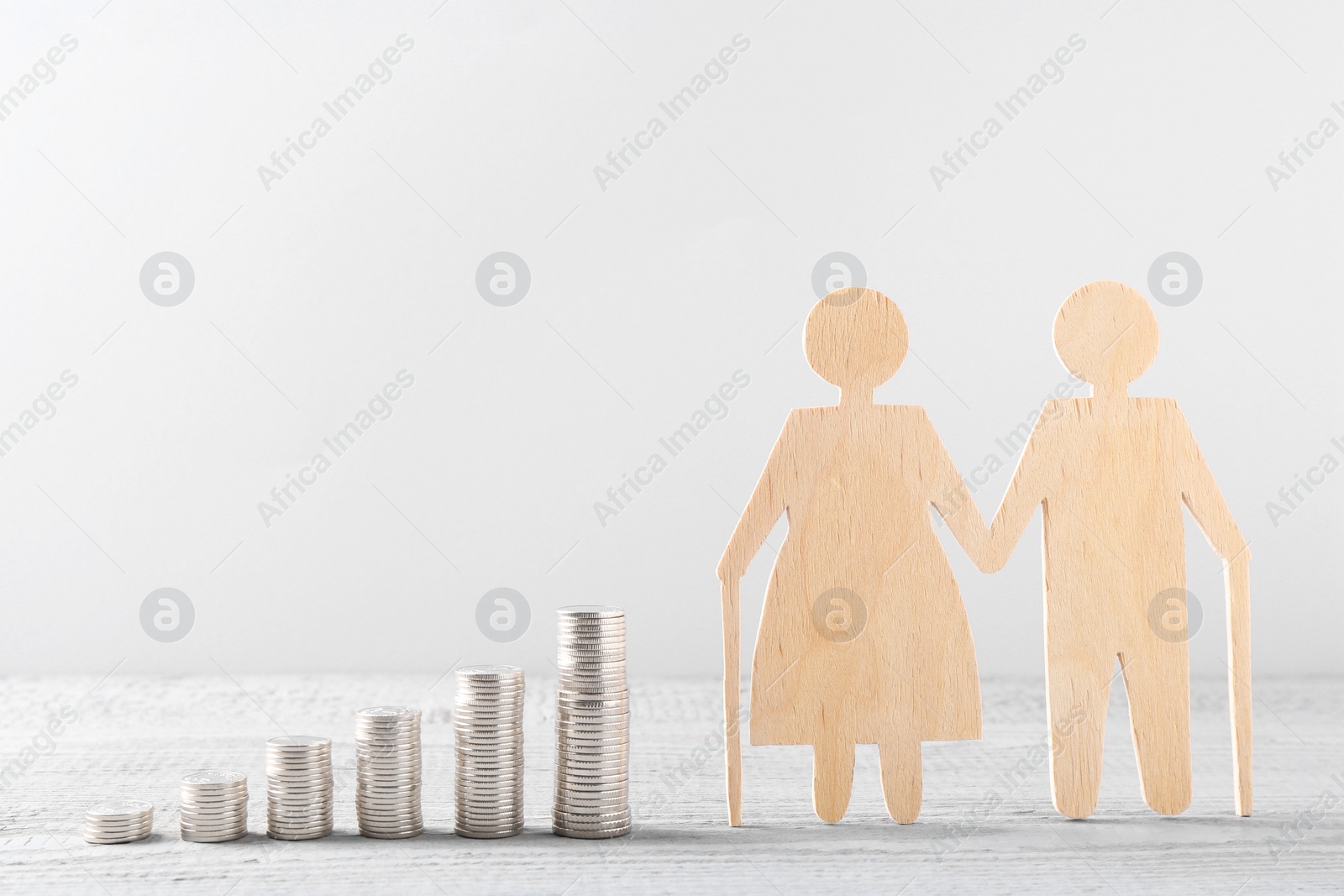 Photo of Pension savings. Figure of senior couple and stacked coins on grey wooden table