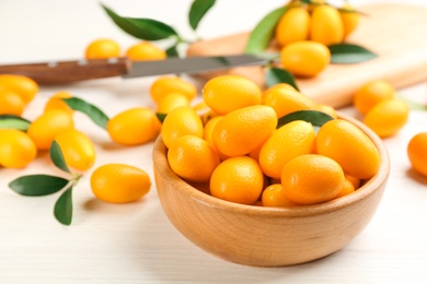Photo of Fresh ripe kumquats with green leaves on white wooden table
