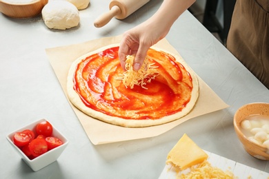 Woman adding cheese to pizza on table