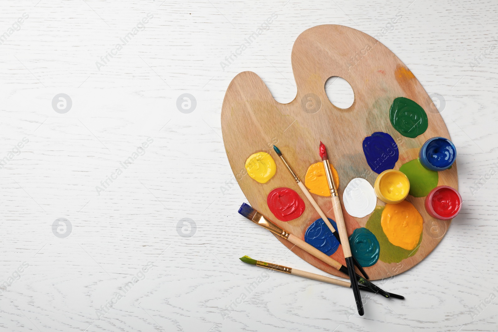 Photo of Wooden palette with colorful paints and brushes on light background, top view