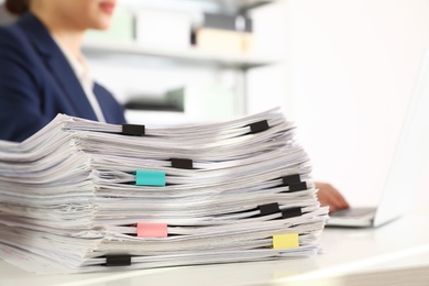 Photo of Stack of documents and woman working with laptop at table in office, closeup