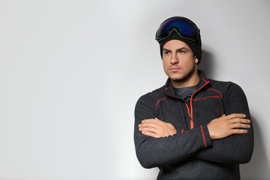 Photo of Man wearing fleece jacket and goggles on light grey background, space for text. Winter sport clothes