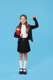 Photo of Happy schoolgirl with book on light blue background