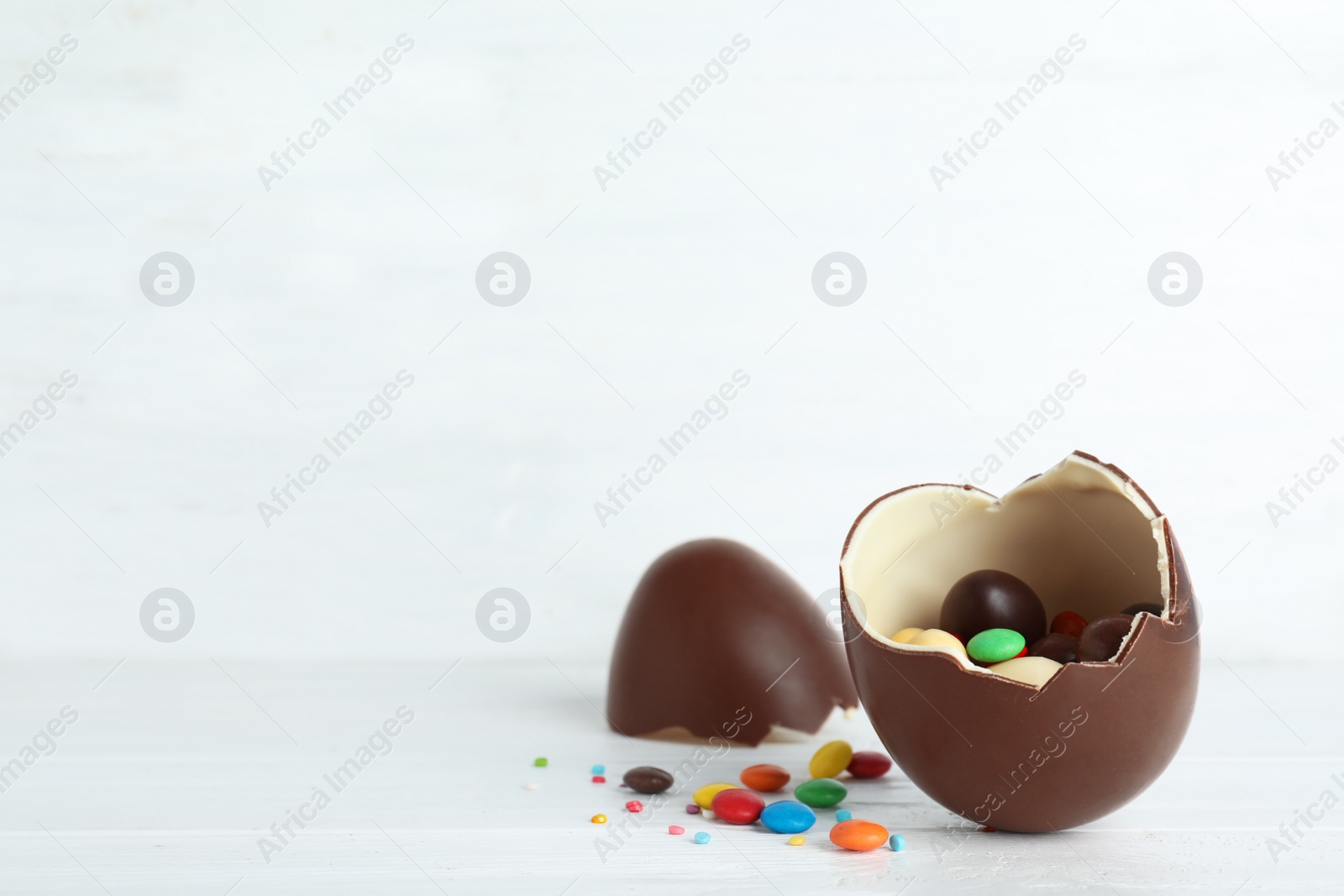 Photo of Cracked chocolate Easter egg with candies on table. Space for text