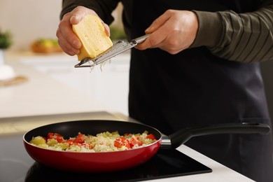 Photo of Cooking process. Man grating cheese into frying pan in kitchen, closeup