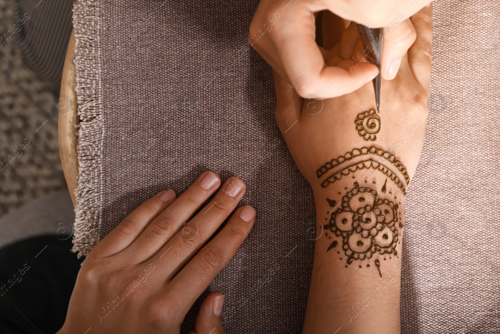 Photo of Master making henna tattoo on hand, top view. Traditional mehndi