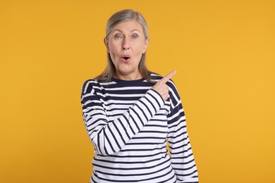 Photo of Surprised senior woman pointing at something on yellow background