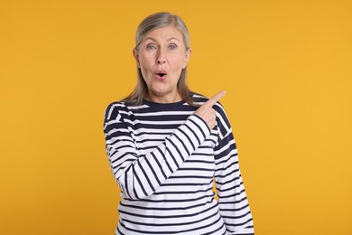 Surprised senior woman pointing at something on yellow background