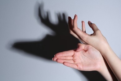 Photo of Shadow puppet. Woman making hand gesture like deer on grey background, closeup