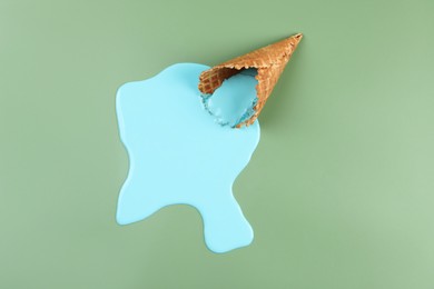 Photo of Melted ice cream and wafer cone on green background, top view